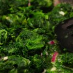 Spinaci freschi in padella, con un cucchiaio di legno, evidenziando la cottura e la perdita di nutrienti.