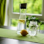 Un bicchiere di acqua fredda accanto a un piatto di cibo, illustrando i rischi di bere durante i pasti.