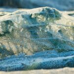 Argilla verde ventilata in polvere, contenuta in un barattolo, con un cucchiaio di legno accanto.
